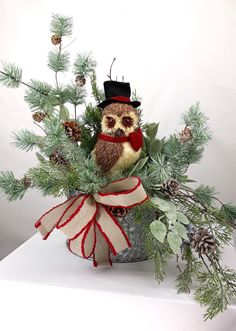 an owl sitting on top of a potted plant with pine cones and evergreen branches