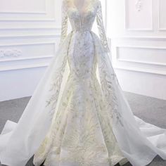 a white wedding dress with long sleeves and a train on display in front of a window