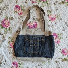 a denim bag sitting on top of a bed covered in pink roses and blue jeans