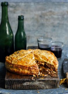 a meat pie is cut in half on a cutting board next to two green bottles