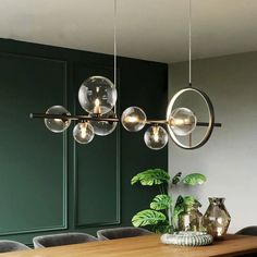 a dining room table with chairs and lights hanging from the ceiling above it, surrounded by greenery