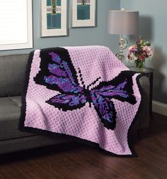 a crocheted blanket with a purple butterfly on it is sitting on a couch