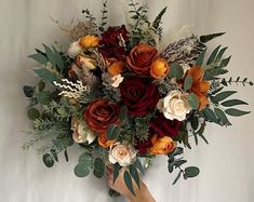 a bridal bouquet with orange and red flowers on it is held up against a white wall