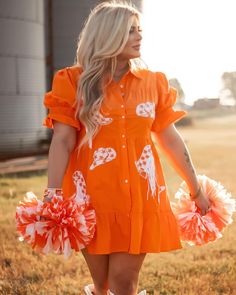 a woman in an orange dress holding two cheerleader pom poms