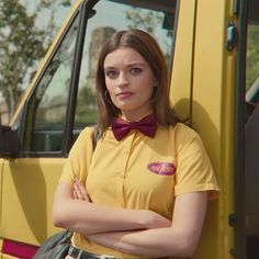 a woman with her arms crossed standing in front of a yellow truck wearing a bow tie