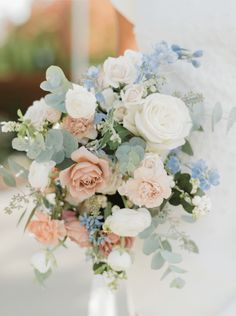 a bridal bouquet with peach and blue flowers in a clear vase on a table