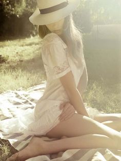 a woman sitting on top of a blanket wearing a white dress and a straw hat