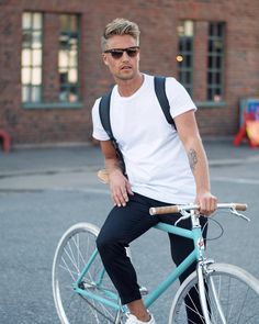 a man in white shirt and black pants riding a blue bike with suspenders on