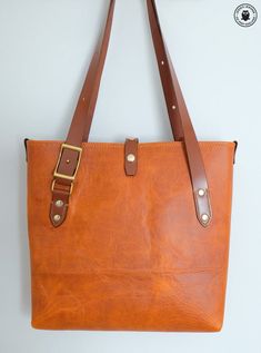 This hand made leather tote bag can have many uses including as a handbag, shopping bag, gym bag, baby items or anything else you can think of!The main body of the bag is made from a single continuous piece of leather for maximum strength and minimal seams. The straps adjust by means of two solid brass conway buckles to suit either shoulder or hand carry (instructions are included, please see photos for measurements).✾ Details:✤ main bag is made from tan coloured cowhide (fully lined with the sa Orange Tote Bucket Bag For Everyday Use, Orange Leather Satchel For Everyday Use, Dark Tan Leather Handled Tote Satchel, Dark Tan Leather Handles Satchel Tote, Orange Bags With Leather Lining For Everyday Use, Waxed Finish Tote Shoulder Bag For Shopping, Waxed Finish Satchel Shoulder Bag For Shopping, Orange Leather Bucket Bag For Everyday Use, Dark Tan Tote Satchel For Everyday Use