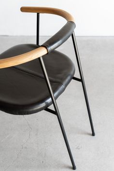 a black leather chair with wooden armrests on concrete flooring and white wall in background