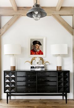 a black dresser with two lamps and a painting on the wall