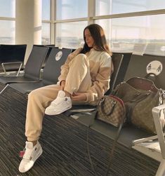 a woman sitting on top of an airport bench next to her purse and handbag