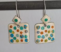 two square shaped earrings with multicolored dots on them hanging from a metal hook