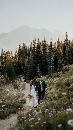 a bride and groom walking through the woods with mountains in the background on their wedding day