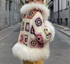 a woman standing on the street wearing a white jacket with colorful crocheted designs