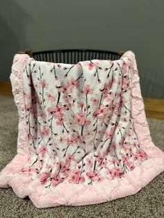 a blanket with pink flowers on it sitting in front of a black and white basket