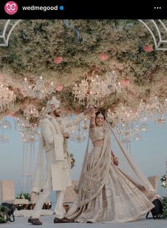 a man and woman dressed in white standing under a chandelier with flowers on it