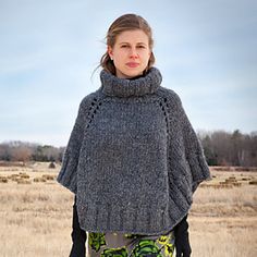 a woman standing in a field wearing a gray ponchle and green leggings