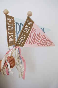 a person holding two paper pennants that say happy first birthday and kindergartie