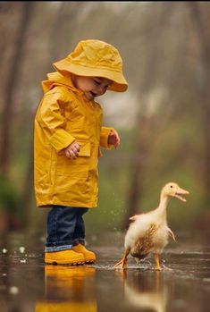 a little boy standing next to a duck in the rain