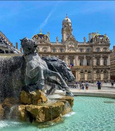 a fountain in front of a large building with a horse statue on it's side