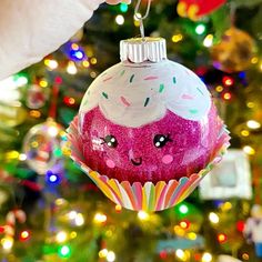 someone is holding up a pink ornament in front of a christmas tree