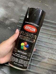 a person holding a black spray can on top of a metal grate with the words krylon in it