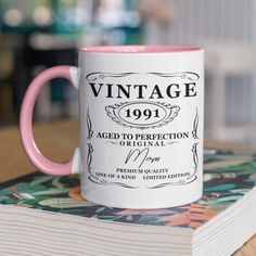 a pink and white coffee mug sitting on top of a table next to a book