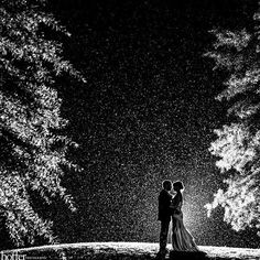 a bride and groom standing in the rain at night