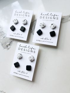 three black and white earrings on top of a marble counter next to an ad for little designs