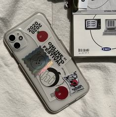 an iphone case with stickers on it sitting next to a package of tissues and a cell phone