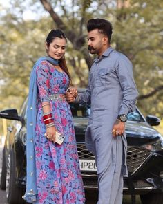 a man and woman standing next to each other in front of a car