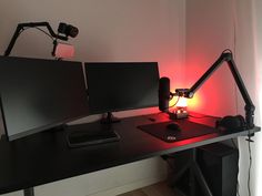 a computer desk with two monitors and a keyboard on it in front of a red light