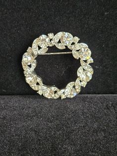 This circle brooch has entwining rows of small rhinestones around large rhinestones that catch all the lights to reflect beauty. There is a signature on the back but I couldn't make it out. Please look at the pictures carefully as this is the item you're purchasing.  I do combine shipping on multiple items. Elegant Round Brooches With Rhinestones, Elegant Round Rhinestone Brooches, Round Rhinestone Brooches For Formal Occasions, Round Formal Brooches With Rhinestones, Formal Round Brooches With Rhinestones, Formal Round Rhinestone Brooches, Crystal Round Brooch For Party, Round Crystal Brooch For Party, Silver Rhinestone Round Brooches