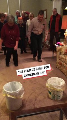 a group of people standing in a living room next to a christmas tree with a sign that reads, the perfect game for christmas day