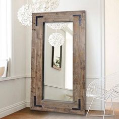 a mirror sitting on top of a wooden floor next to a white chair and window