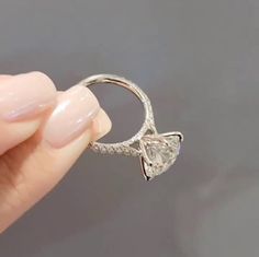 a woman's hand holding an engagement ring with a heart shaped diamond on it