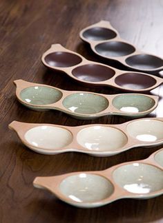 five ceramic spoons lined up on a wooden table with black and white dishes in them