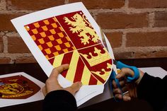 a person is cutting out some paper with scissors on a table next to a brick wall