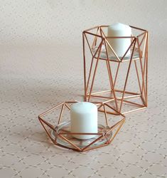 two white candles are sitting in geometric glass holders