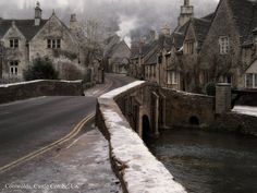 a street with snow on the ground and houses in the background, along with a river running through it