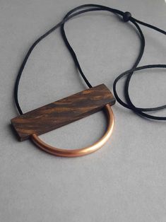 Minimalist wood + copper semircle necklace. Handmade from a beautiful, rich and highly figured piece of walnut wood. Threaded onto a simple black satin (2mm) cord for a contemporary look. The wood has been sealed with organic beeswax to enhance the natural colour and grain. Looks great at a longer length but the charred wood slider bead means that it can be worn long or shorter. The wood is 6.5cm x 1.7cm, 4mm thick. Light in weight and easy on the eye. The copper has been sealed but may tarnish Wooden Jewelery, Simple Jewellery, Charred Wood, Contemporary Necklace, Satin Noir, Wood Necklace, Wire Pendant, Wood Jewellery, Simple Jewelry