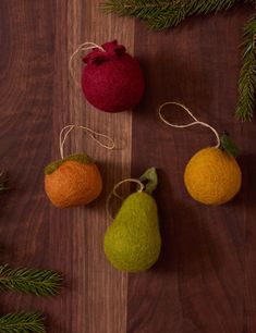 three felt pears and two oranges hanging from twine strings on a wooden table