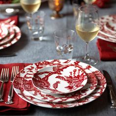 red and white dinnerware set on a table with wine glasses, silverware and napkins