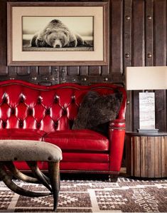 a red leather couch sitting in front of a painting on the wall next to a table