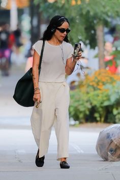 a woman walking down the street while holding a cell phone in one hand and headphones in another