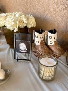 a table topped with candles and pictures next to vases filled with white flowers on top of a cloth covered table