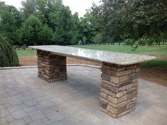 a stone bench sitting on top of a brick walkway next to a lush green park