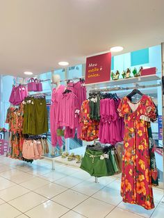 clothes are on display in a store with pink and green shirts hanging from the rack