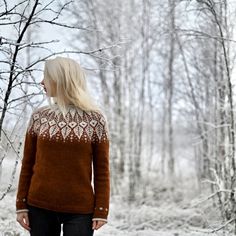 a woman standing in the snow with her back turned to the camera, wearing a brown sweater and black jeans